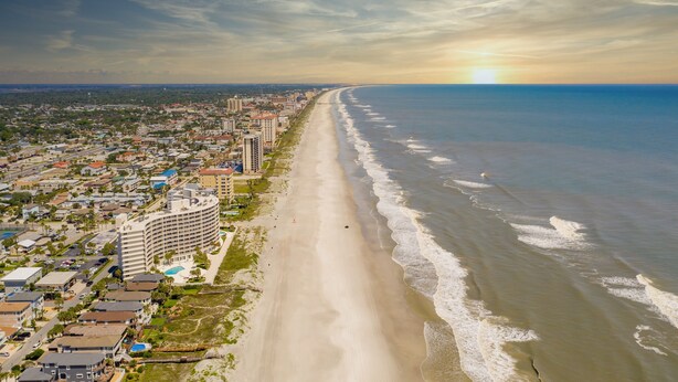 A coastal cityscape with a long beach, a large hotel with a curved facade, and a clear sky.