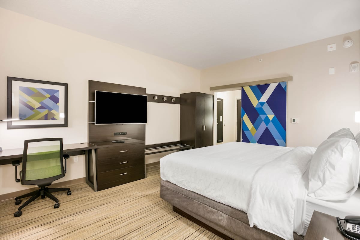 Habitación de hotel con cama, escritorio, silla, televisor y obras de arte en las paredes.