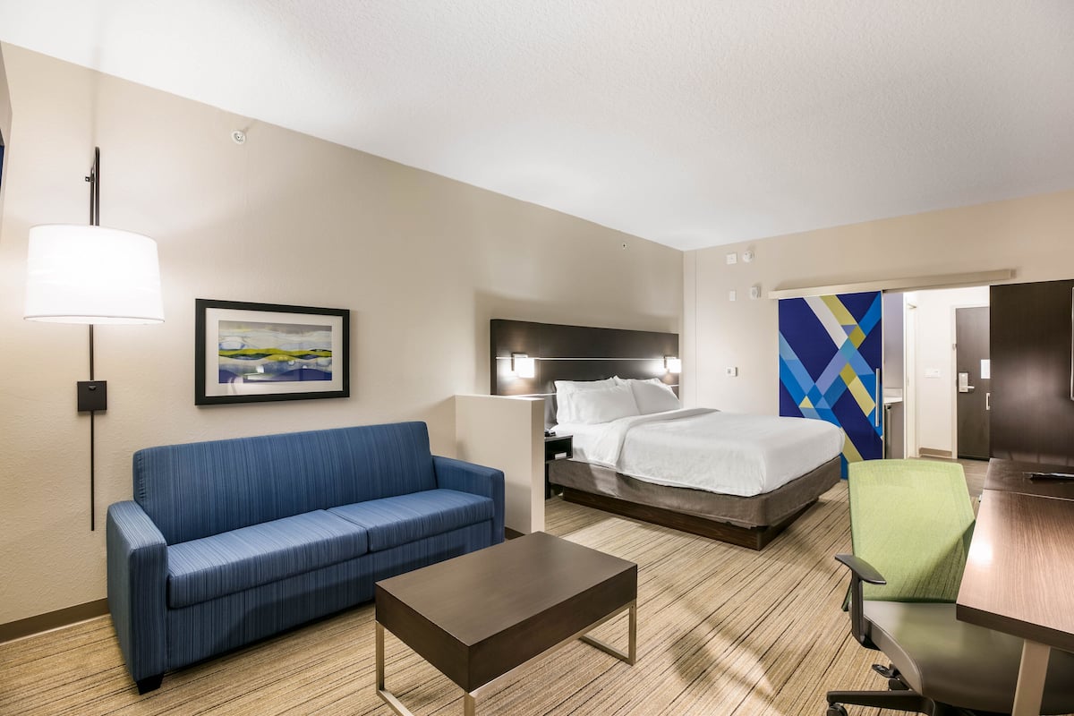 Un cuarto de hotel con una cama, un sofá azul, una mesa de centro de madera, una silla verde y un cuadro en la pared.