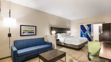 A hotel room with a bed, a blue sofa, a wooden coffee table, a green chair, and a painting on the wall.