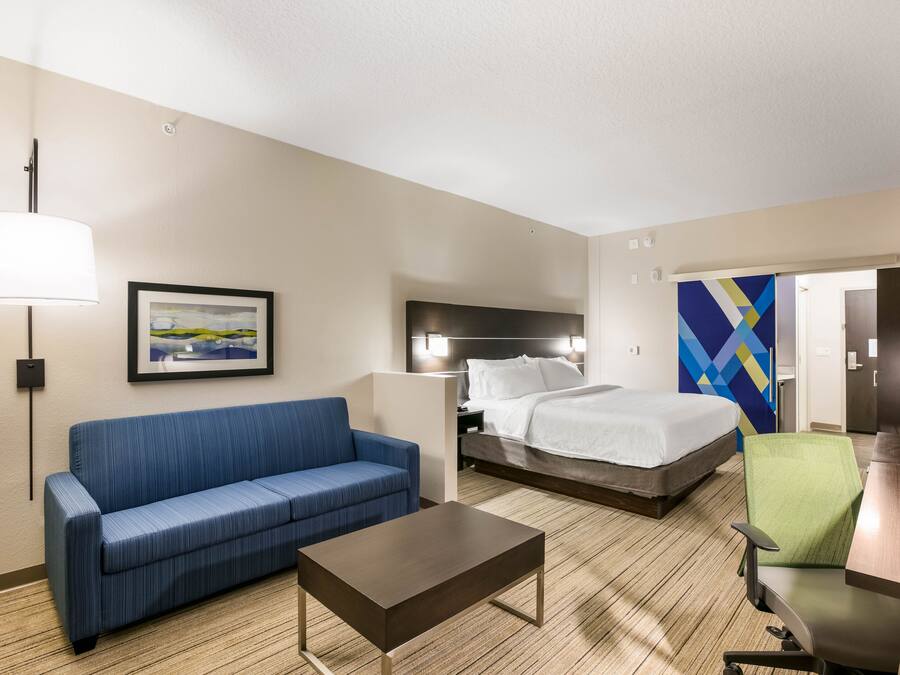 A hotel room with a bed, a blue sofa, a wooden coffee table, a green chair, and a painting on the wall.