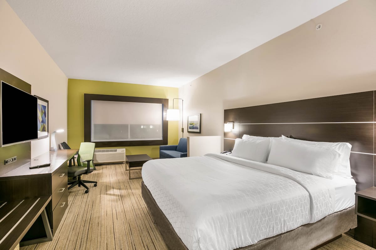 Una habitación de hotel con una cama grande, un escritorio con computadora, una silla y un televisor.