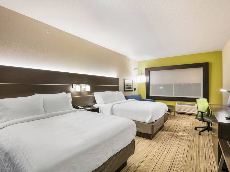 A hotel room with two beds, a desk, a chair, a TV, and a large window.