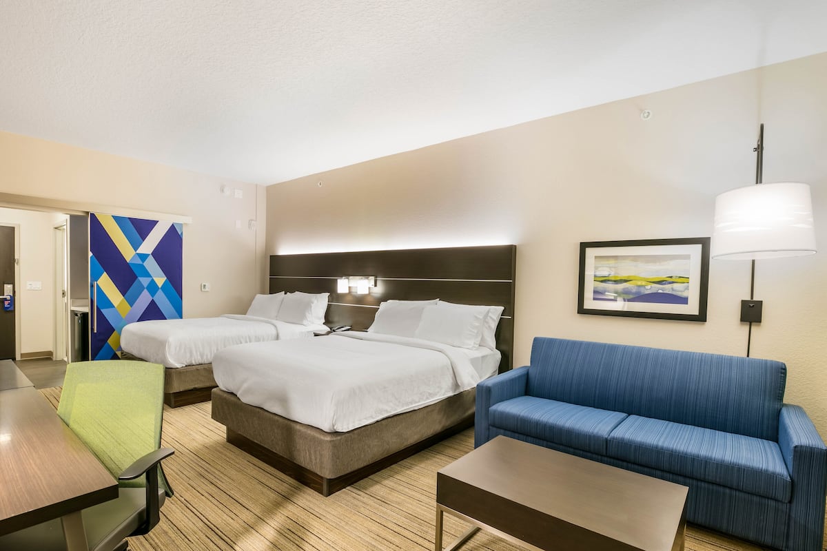 Una habitación de hotel con dos camas, un sofá azul, un escritorio y una lámpara.