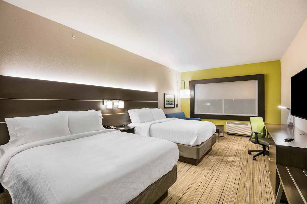 Habitación de hotel con dos camas, un escritorio, una silla, un televisor y un ventanal grande.