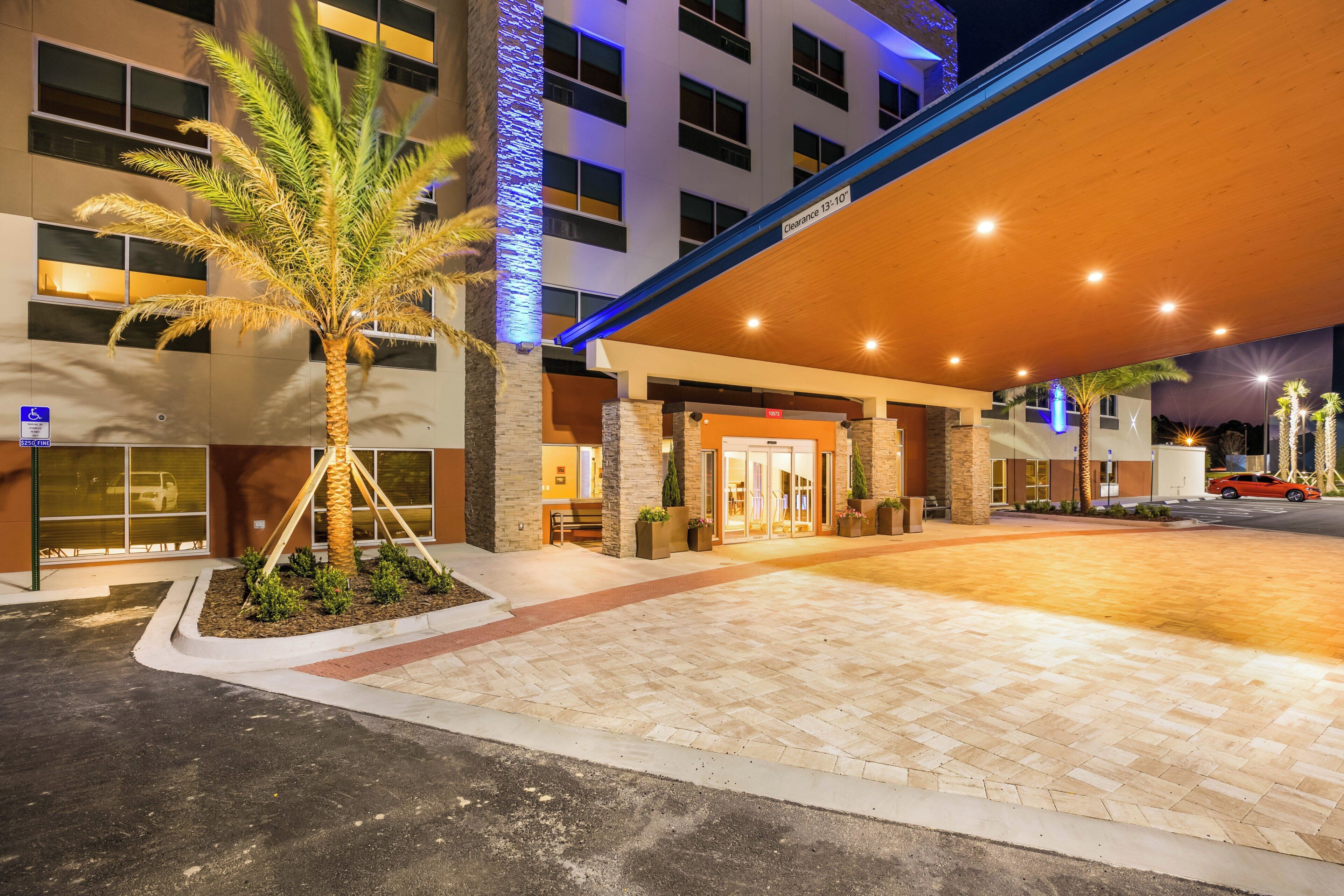L’entrée d’un hôtel, avec un passage couvert, des palmiers et un espace de stationnement.