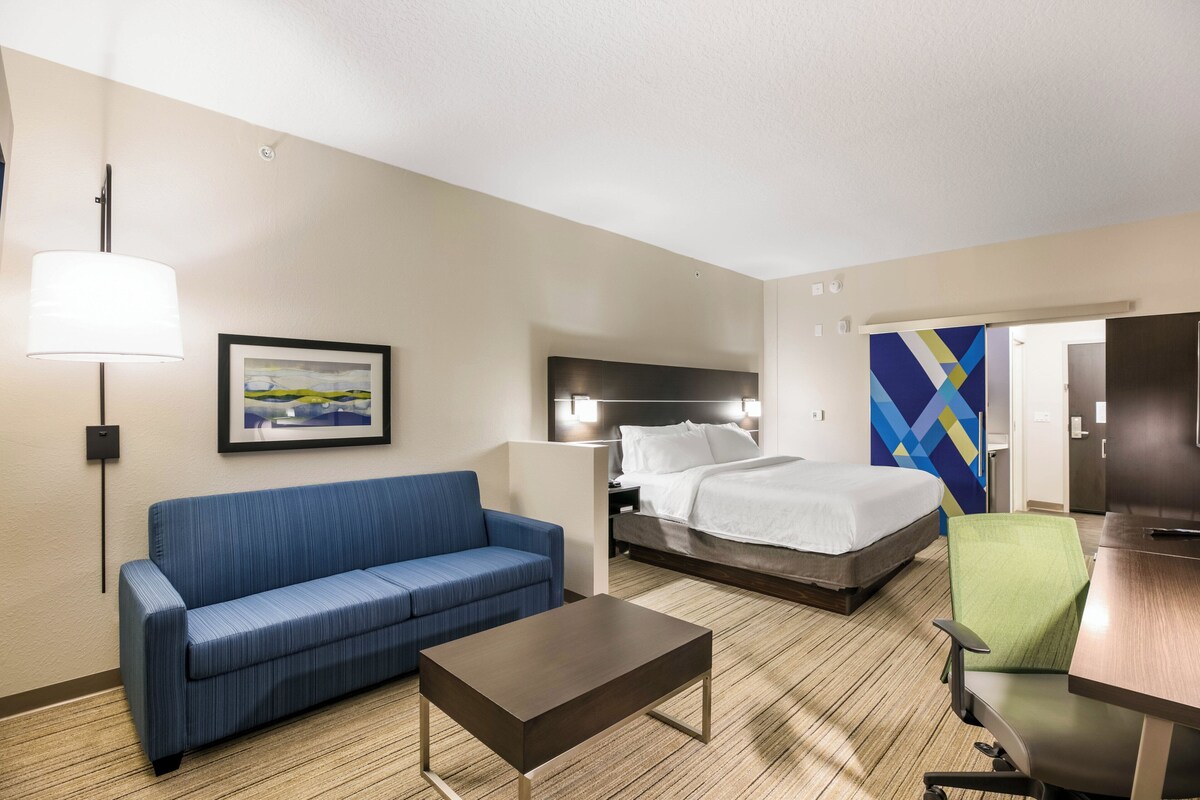 Een hotelkamer met een bed, een blauwe bank, een bureau, een stoel, een lamp en een schilderij aan de muur.