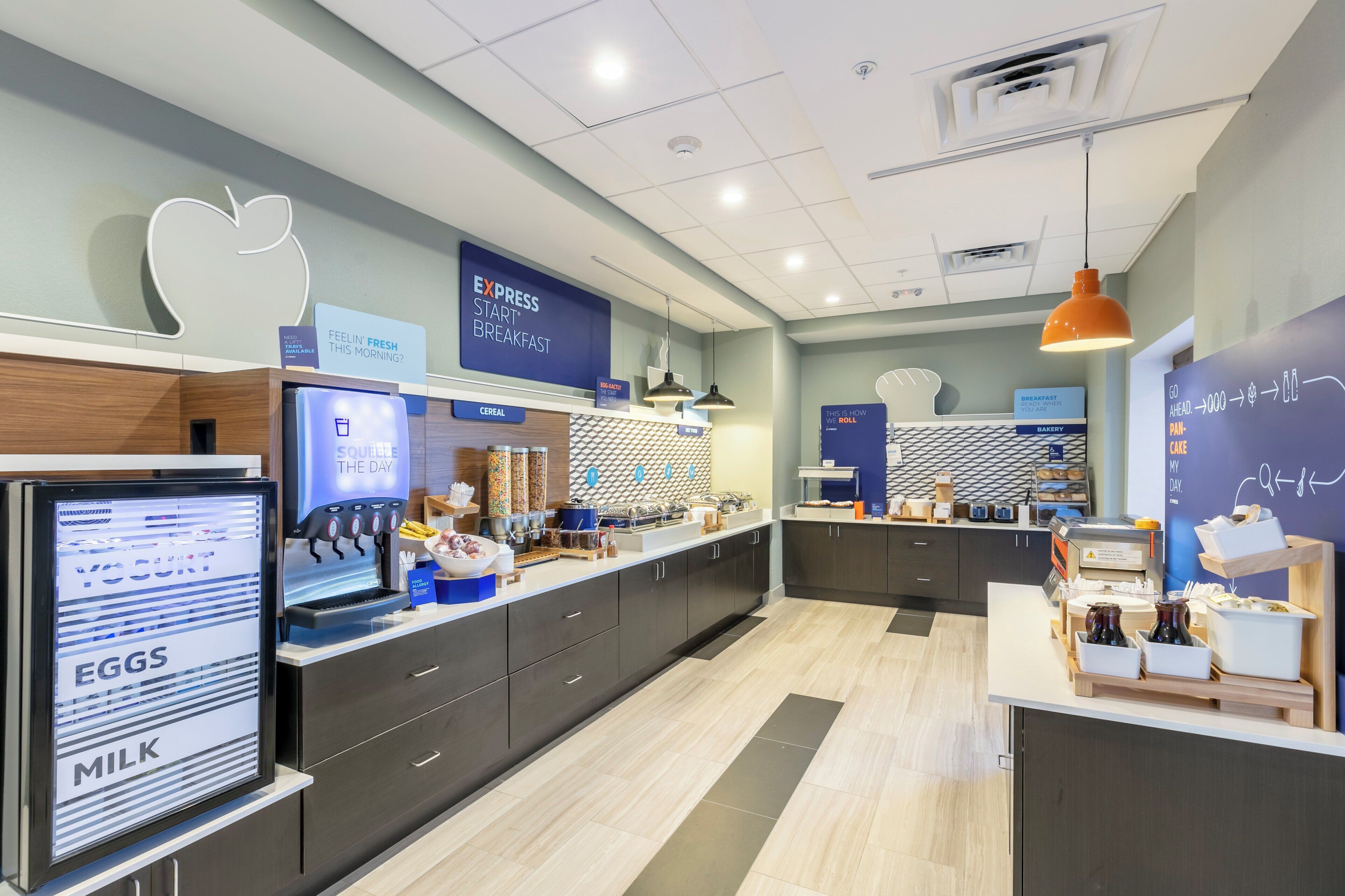 Un espace moderne dédié au petit-déjeuner, avec un buffet où les clients peuvent se servir eux-mêmes, un coin boulangerie et un panneau indiquant si le petit-déjeuner est servi.