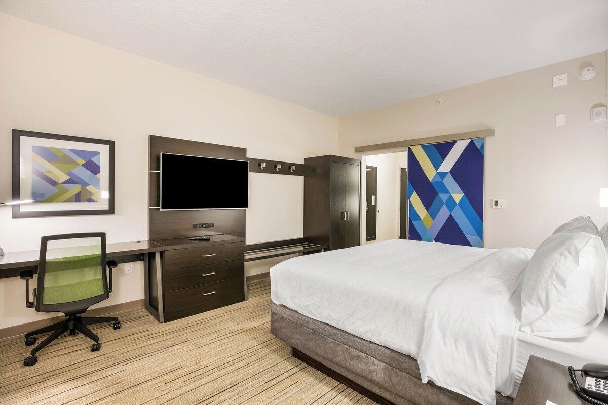 Een hotelkamer met een bed, bureau, stoel, televisie, kledingkast en kunst aan de muren.