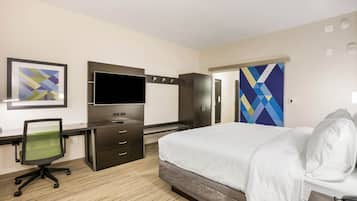 A hotel room with a bed, desk, chair, TV, wardrobe, and artwork on the walls.