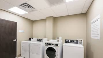 A laundry facility with four washing machines, a sign indicating guest laundry use, and a mechanical room sign.