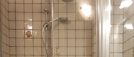 A shower with a glass door, a sink, and tiled walls.