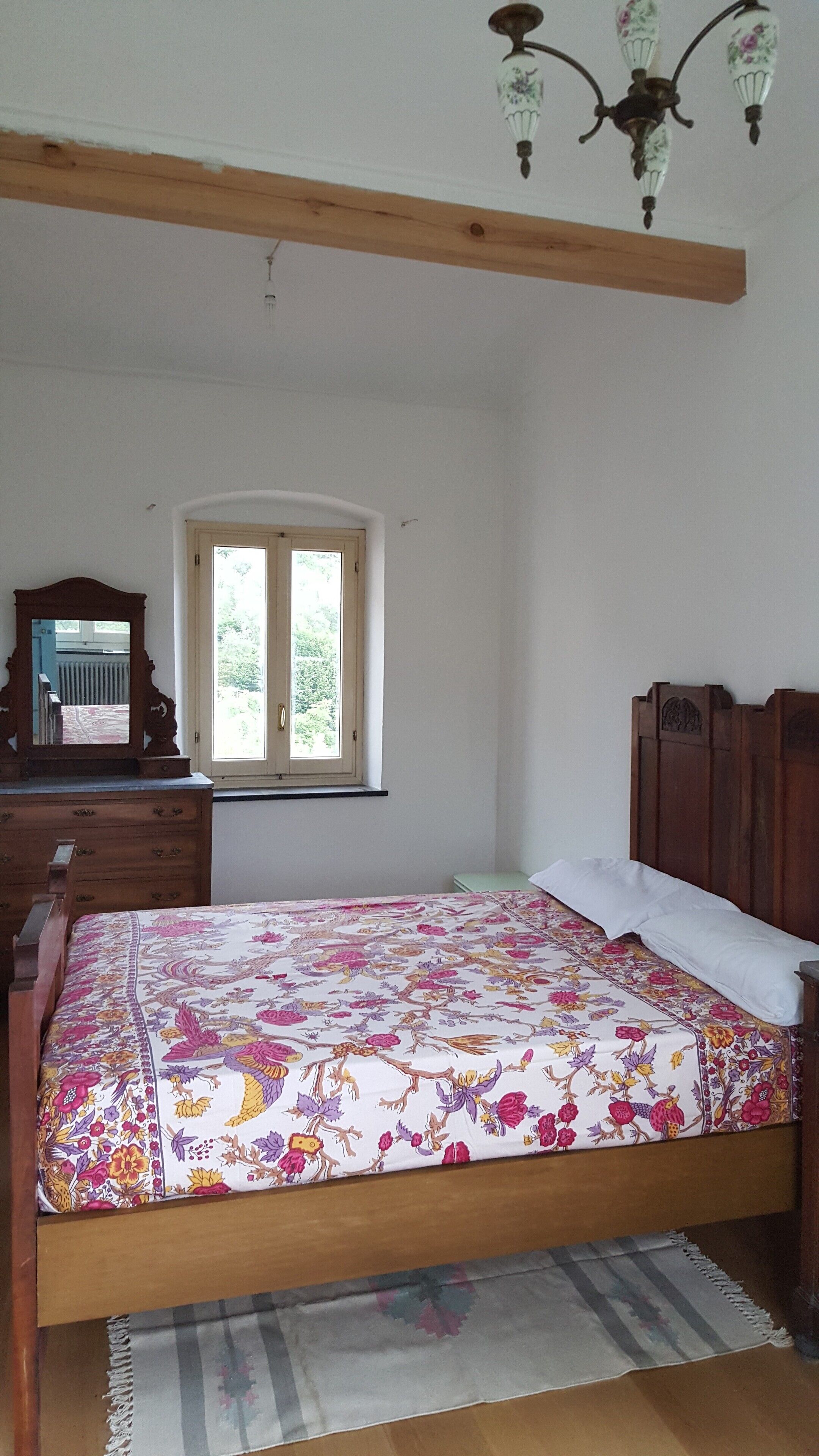 Une chambre à coucher avec un lit en bois, une commode, un miroir, une fenêtre et un lustre.