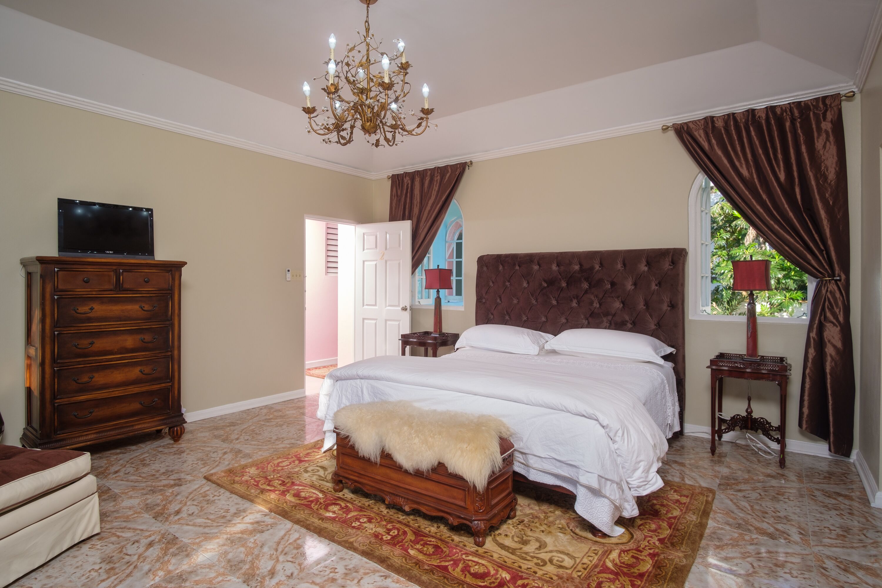 A bedroom with a large bed, a dresser, a television, and a chandelier.