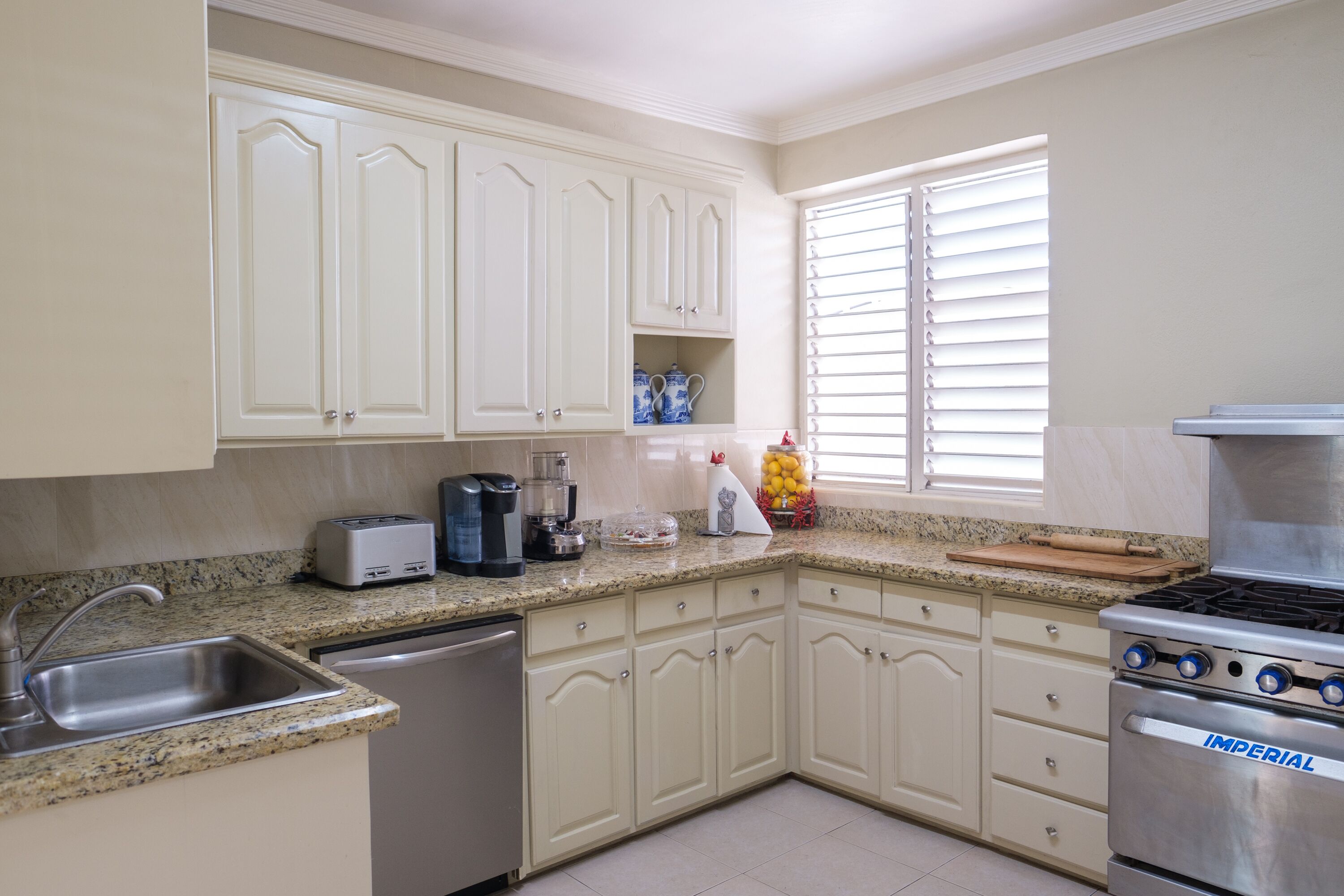 A kitchen with white cabinets, a stainless steel sink, a coffee maker, and a stove.