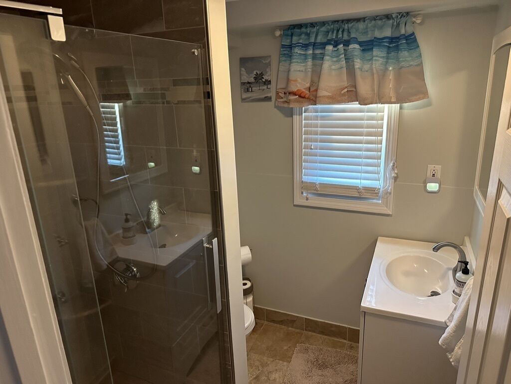 Ein Badezimmer mit einer Duschkabine, einem Waschbecken und einem Fenster mit Jalousien.
