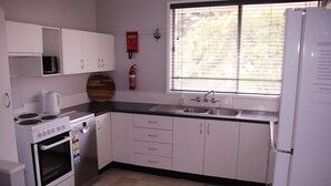 Une cuisine avec des meubles blancs, une cuisinière, un four à micro-ondes, un évier et une fenêtre avec des stores.