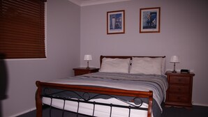 Une chambre à coucher avec un lit en bois, deux tables de chevet et deux lampes fixées au mur.