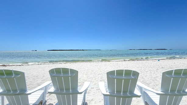 Een strand met witte stoelen gericht op de oceaan, heldere lucht en rustig water.