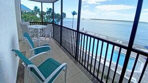 Een balkon met een tafel en stoelen, met uitzicht op een zwembad en de zee.