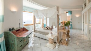 Un dormitorio con cama con dosel, cómoda de madera, mesita de noche con lámpara y vistas al mar.