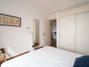 A hotel room with a bed, a mirror, a wardrobe, and a kitchenette in the background.