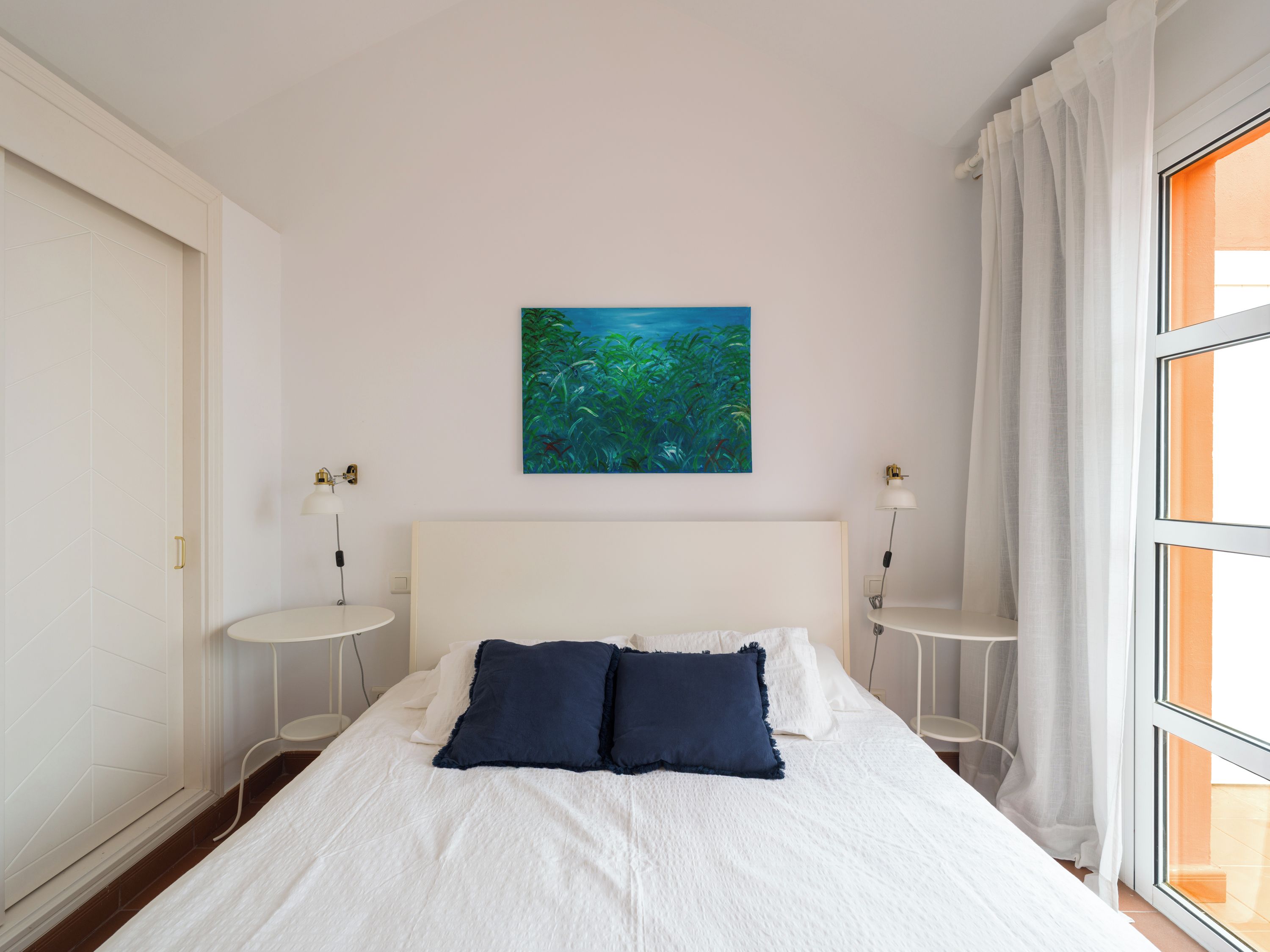 Una camera da letto con un letto, due comodini, un quadro appeso e una finestra con tende.
