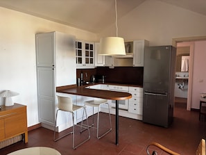 A kitchen with white cabinets, a stainless steel refrigerator, a wooden dining table, and two bar stools.