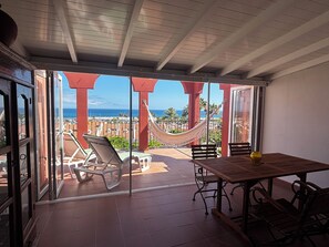 A balcony with a view of the ocean, a hammock, and outdoor seating.
