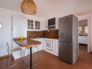 A modern kitchen with white cabinets, a stainless steel refrigerator, a built-in oven, and a round dining table with bar stools.
