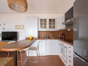 Une cuisine moderne avec des armoires blanches, un réfrigérateur en acier inoxydable, un four encastré et un coin repas comprenant une table et des chaises en bois.