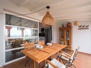 Un coin repas avec une table et des chaises en bois, un luminaire suspendu et une vue à travers une porte vitrée.