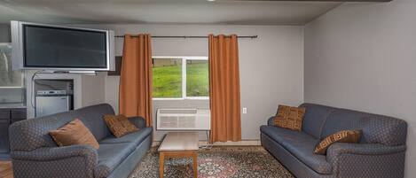En stue med to sofaer, et fladskærms-tv, et lille bord og en tæppe med et mønster.
