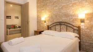 A bedroom with a stone wall, a bed with white linens, two bedside lamps, and a wooden nightstand.