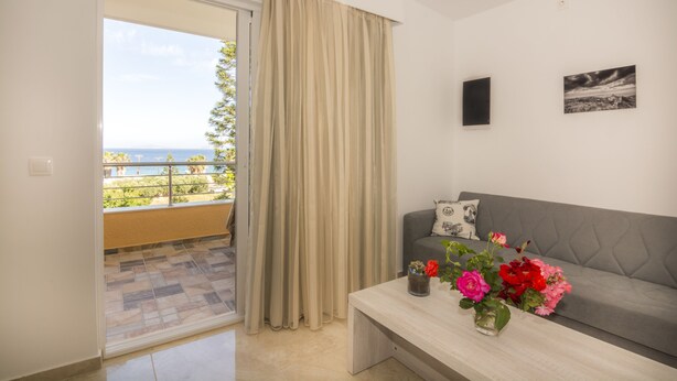 A modern living room with a grey sofa, a coffee table with flowers, and a view of the outdoors through a sliding door.