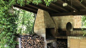 An outdoor stone oven with a chimney, surrounded by stacked firewood and a wooden cabinet. - Beautiful stone country villa in the hills (Casaprota (Rieti))
