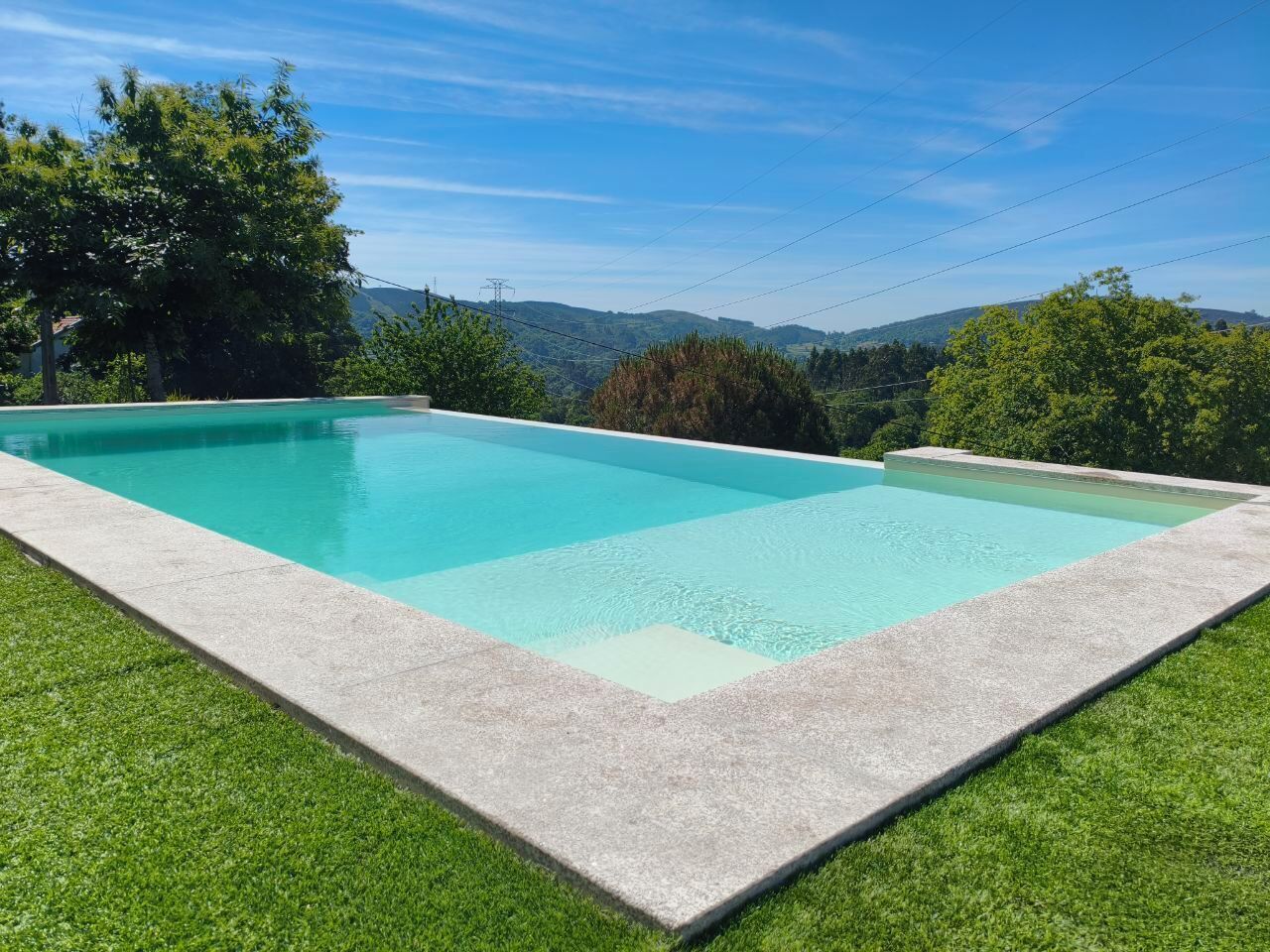 A rectangular swimming pool with a concrete edge, surrounded by well-maintained grass.