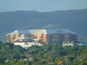Ein mehrgeschossiges Hotel mit flachem Dach und Balkonen, umgeben von üppiger Vegetation und Hügeln im Hintergrund.