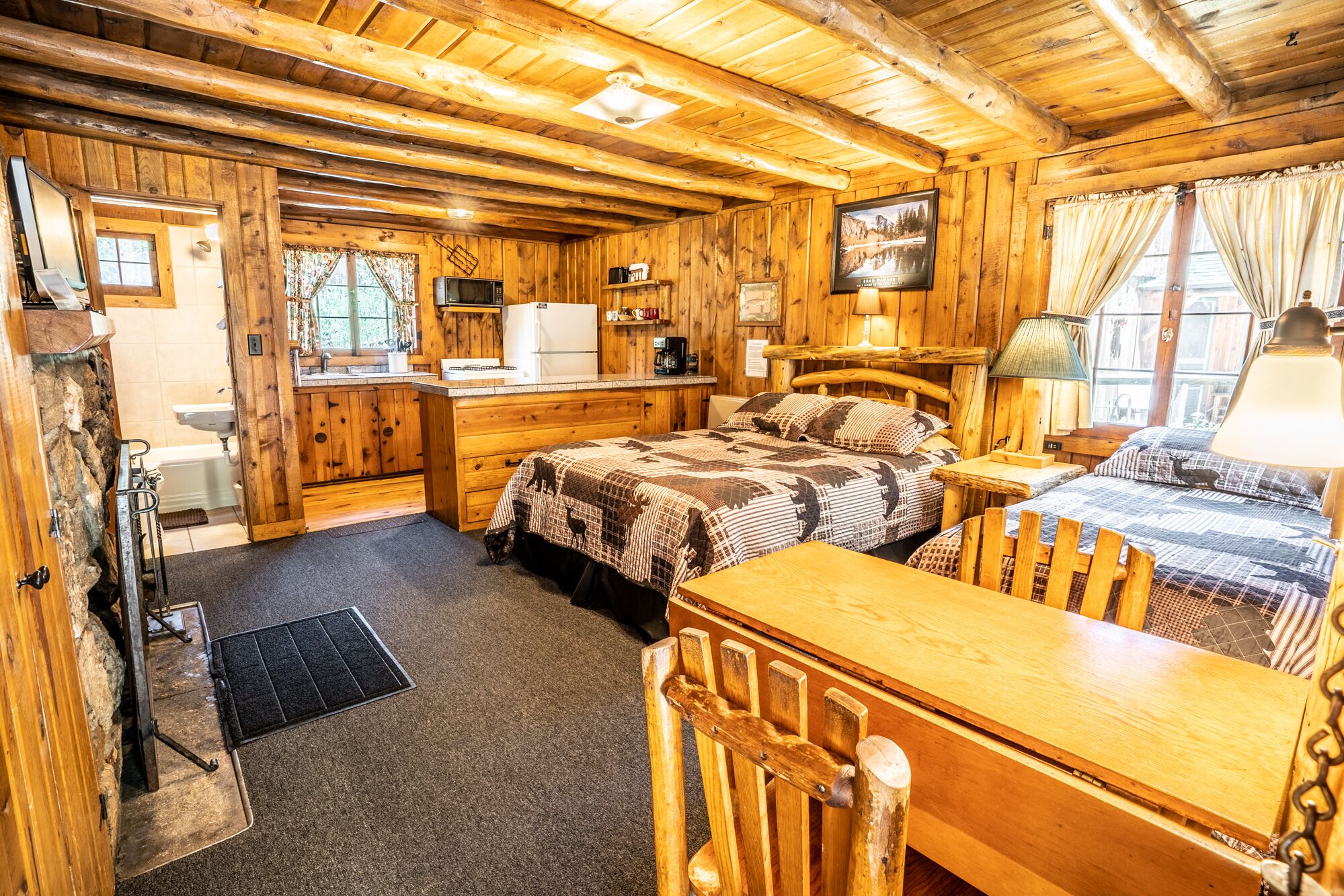 Habitación tipo cabaña de troncos con cama, escritorio, silla, kitchenette y baño.