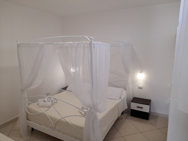 Un dormitorio ordenado con una cama con dosel, una mesita de noche y una lámpara de pared.