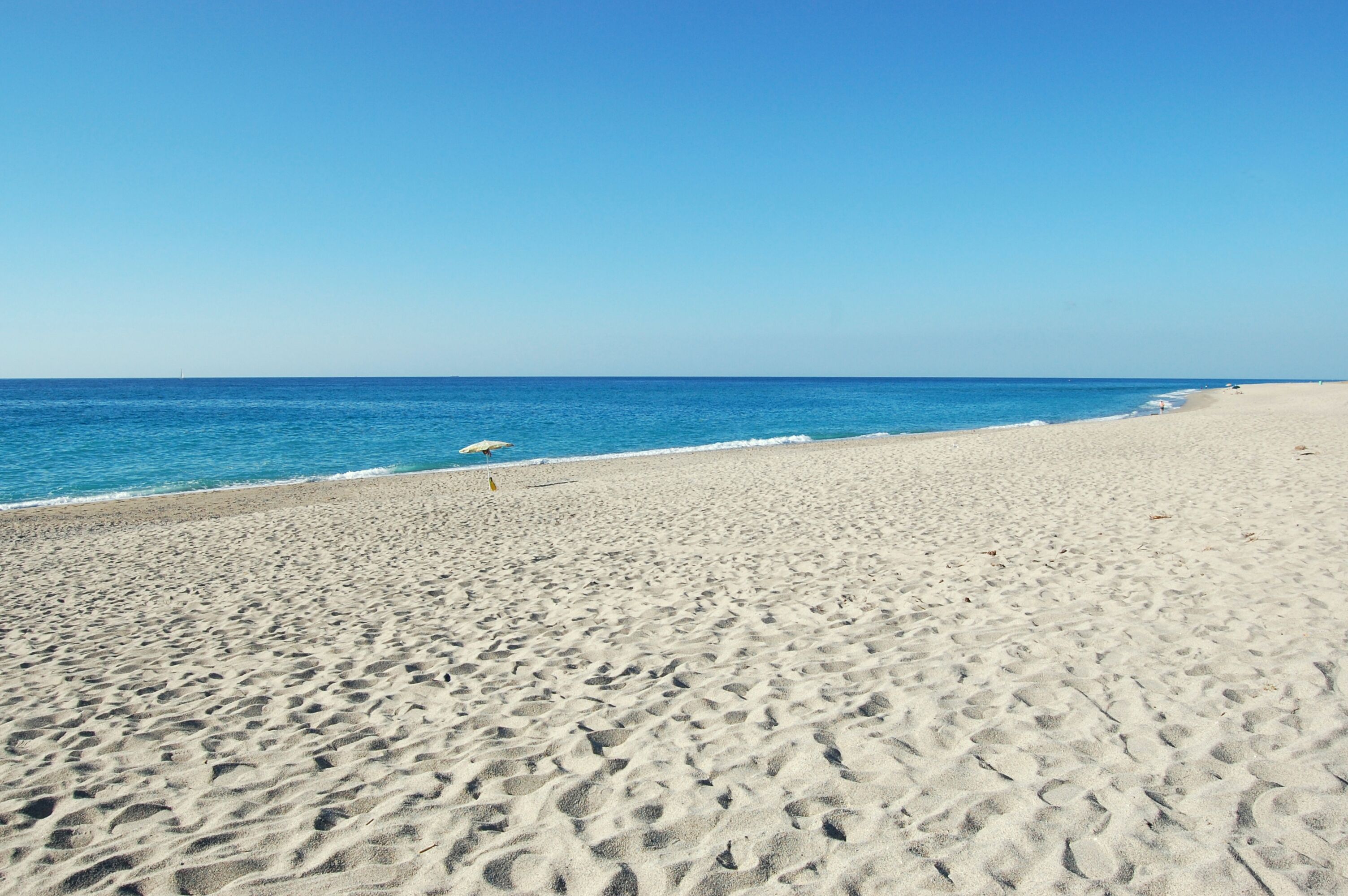 A wide sandy beach with a clear blue sky and calm sea.