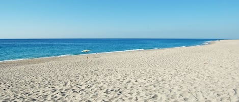 A wide sandy beach with a clear blue sky and calm sea.
