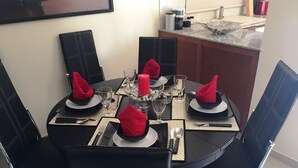 A dining table set for four with black chairs, red napkins, and a central candle.