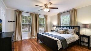 Une chambre à coucher comprenant un lit, un ventilateur de plafond, deux tables de chevet avec des lampes, une commode et une fenêtre avec des rideaux.