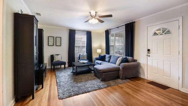 Un salon avec un ventilateur de plafond, un canapé, une table basse, un meuble de couleur foncée et une porte avec une fenêtre.