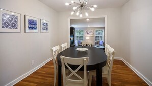 Une salle à manger avec une table noire et des chaises blanches, un lustre et des œuvres d’art encadrées accrochées au mur.