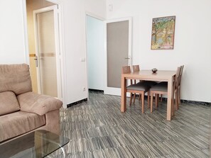 Un salon comprenant un canapé, une table basse en verre, une table à manger avec des chaises et un tableau accroché au mur.