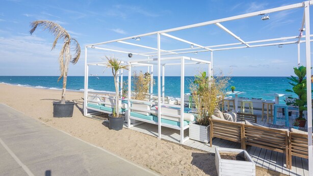 A beachside patio with white wooden furniture, potted plants, and a view of the ocean.