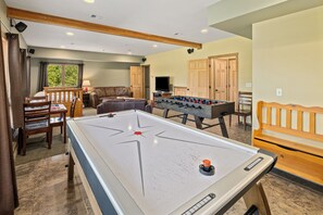 A room with a foosball table, a pool table, a sofa, and a television.
