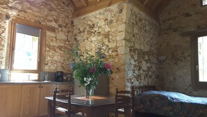 A rustic room with stone walls, a wooden dining table with chairs, a bed with a patterned bedspread, and a window with a view. - Small stone house of the most unusual in the country (Habas)